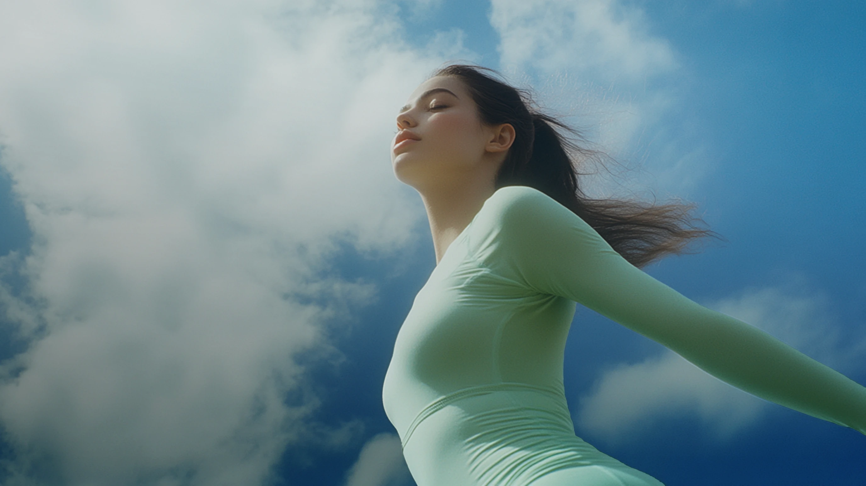 A fit brunette girl in a green workout set, sun rays hitting her face against the sky.