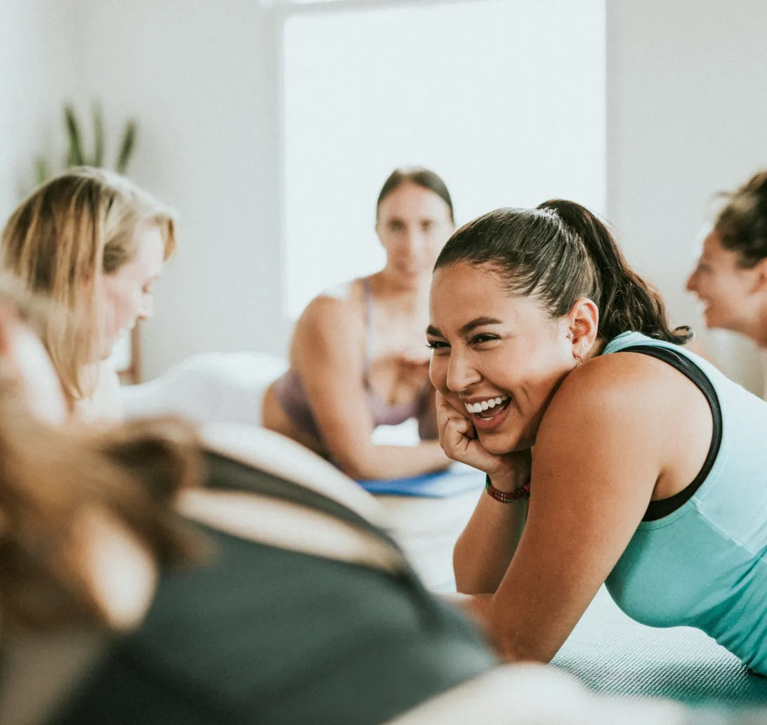 A yoga class with a focus on a smiling girl on her yoga mat, slight blur on other attendees.